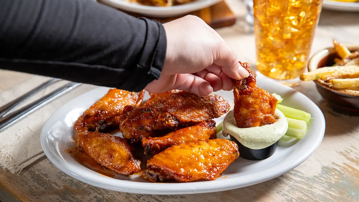 Person dunking chicken wing in sauce.