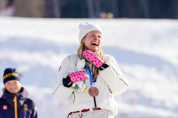 Jessie Diggins of the United States celebrates after winning the bronze medal, while gold medalist Frida Karlsson of Sweden looks on, after the women's 10-km cross-country skiing interval start free at the 2026 Winter Olympics on Thursday, Feb. 12, 2026, in Tesero, Italy. (AP Photo/Kirsty Wigglesworth)