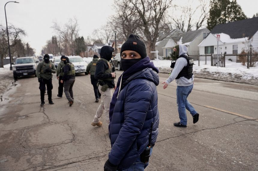 A federal agent in plain clothes looks on a group conducts immigration enforcement in Minneapolis, Minnesota, on February 5, 2026.