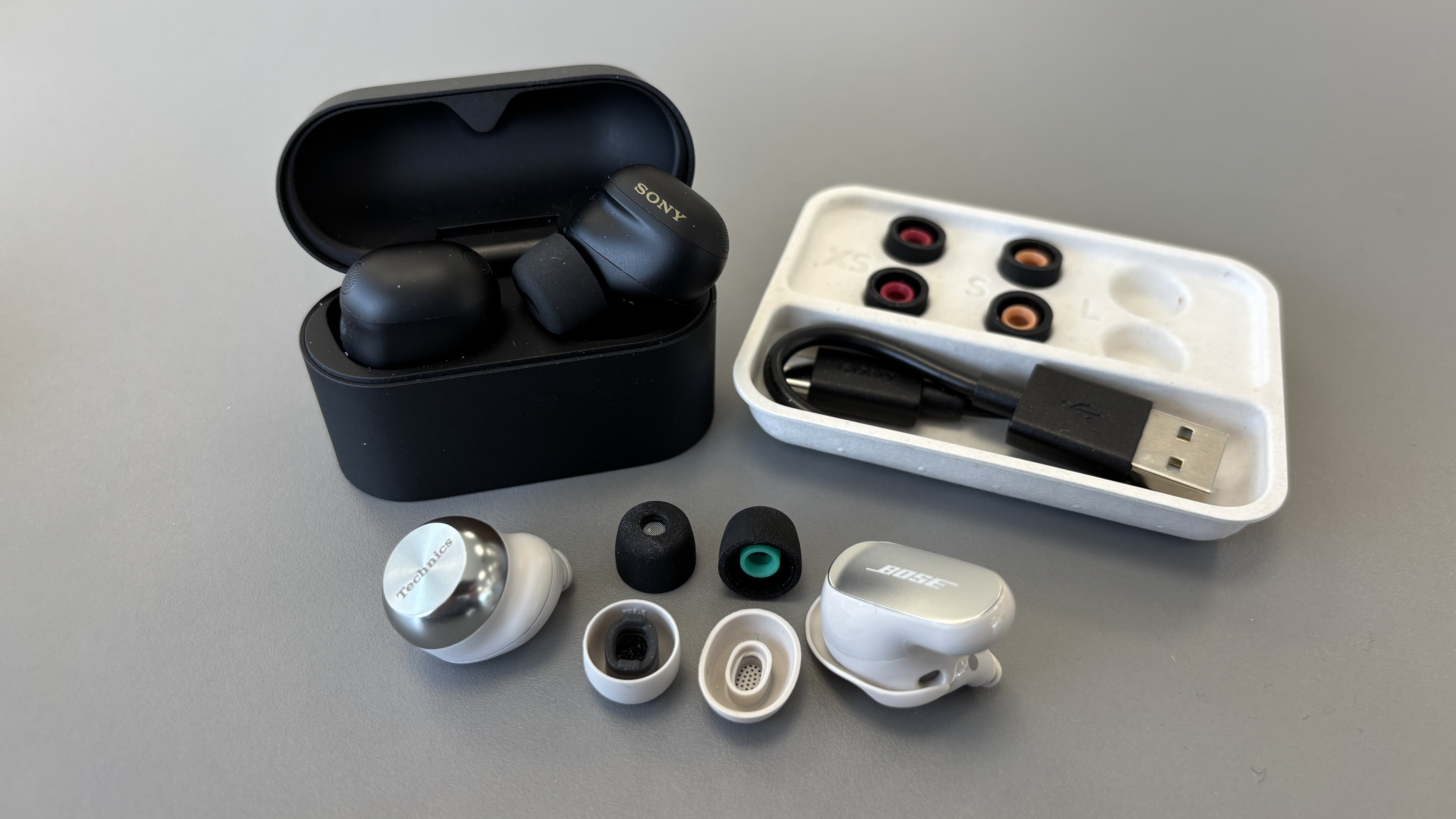 Sony WF-1000XM6 wireless earbuds on a table next to Bose and Technics earbuds with the eartips taken off