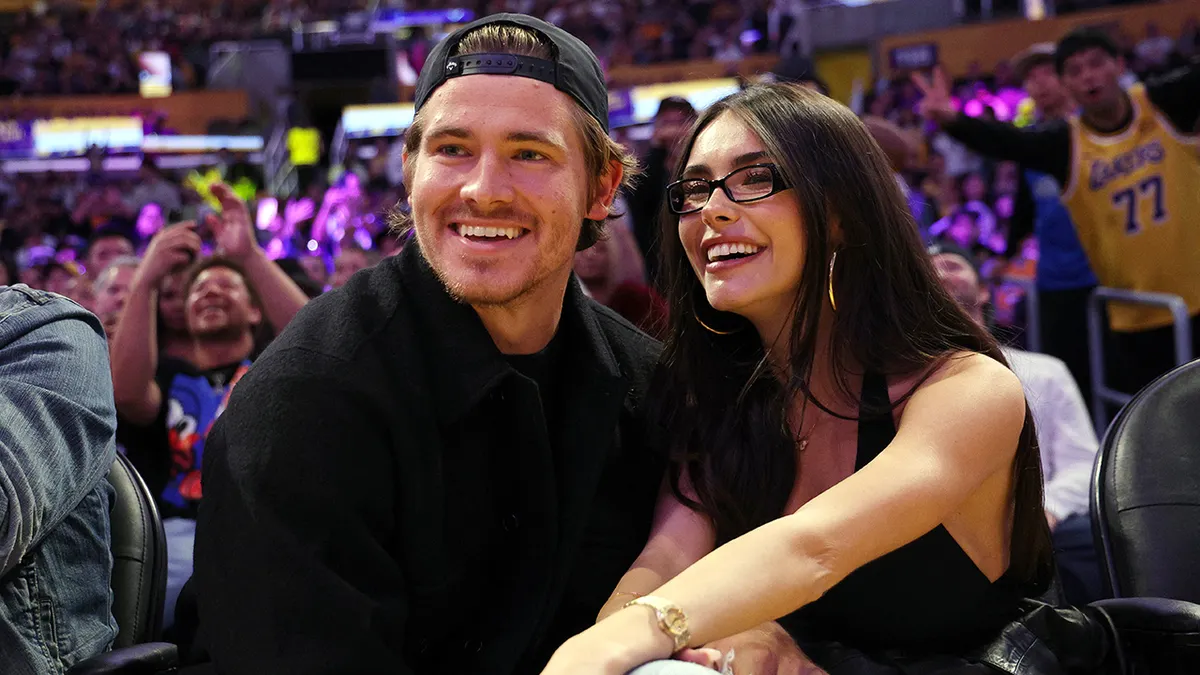 Quarterback Justin Herbert and Madison Beer seated courtside at a basketball game.