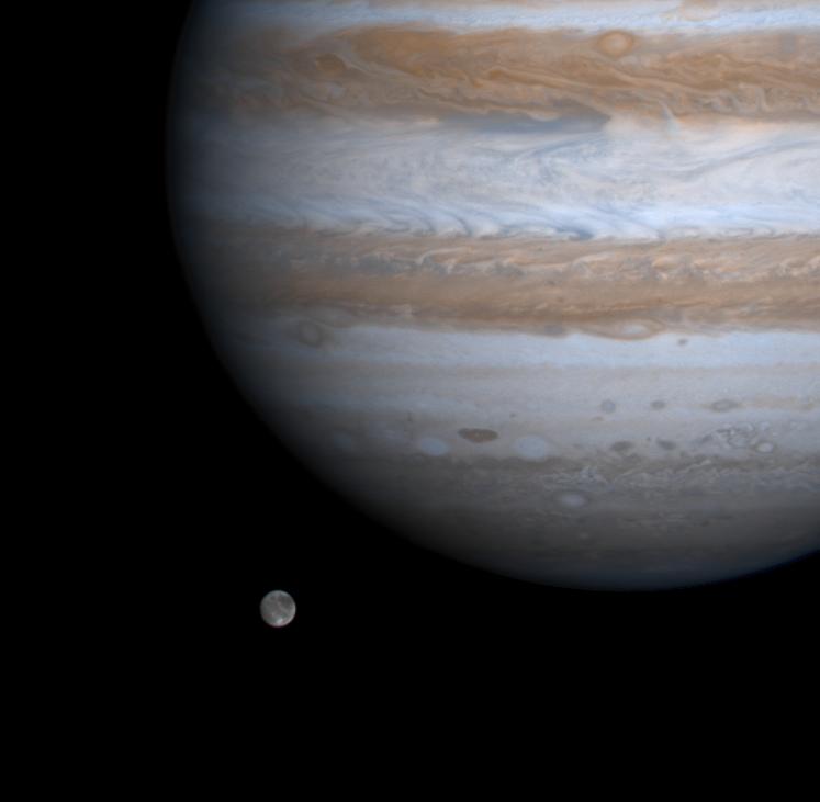 Part of Jupiter with its dark and light bands and a small mottled moon to the lower left.