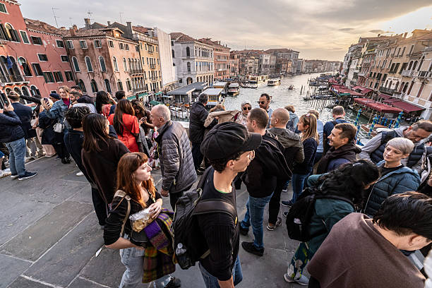 Crowds of tourists on Rialto Bridge overlooking the Grand Canal with boats and historic buildings in Venice
