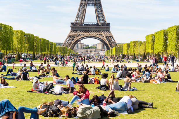 People relaxing on grass at Champ de Mars with the Eiffel Tower in the background on a sunny day.