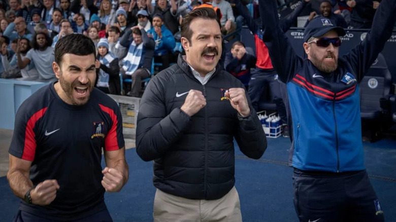 Roy Kent (Brett Goldstein), Ted Lasso (Jason Sudeikis), and Willis Beard (Brendan Hunt) cheer on the sidelines in Ted Lasso