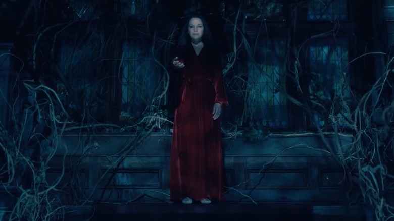 A ghostly Olivia Crain (Carla Gugino) holds out her hand while standing in an overgrown room in The Haunting of Hill House