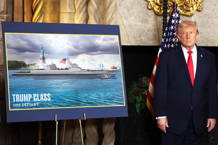 Donald Trump stands next to a signboard with an image of a battleship inside a room at Mar-a-Lago.