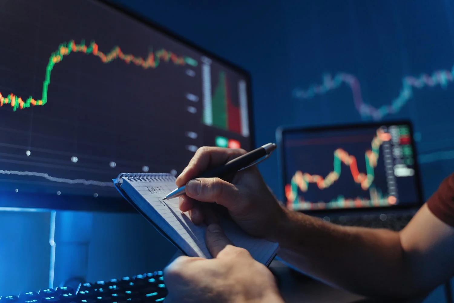 No face image of male hands writing numbers in notepad after analyzing diagram of crypto currency market at his pc, predicting patterns of money flow, inventing new strategy avoiding high risks