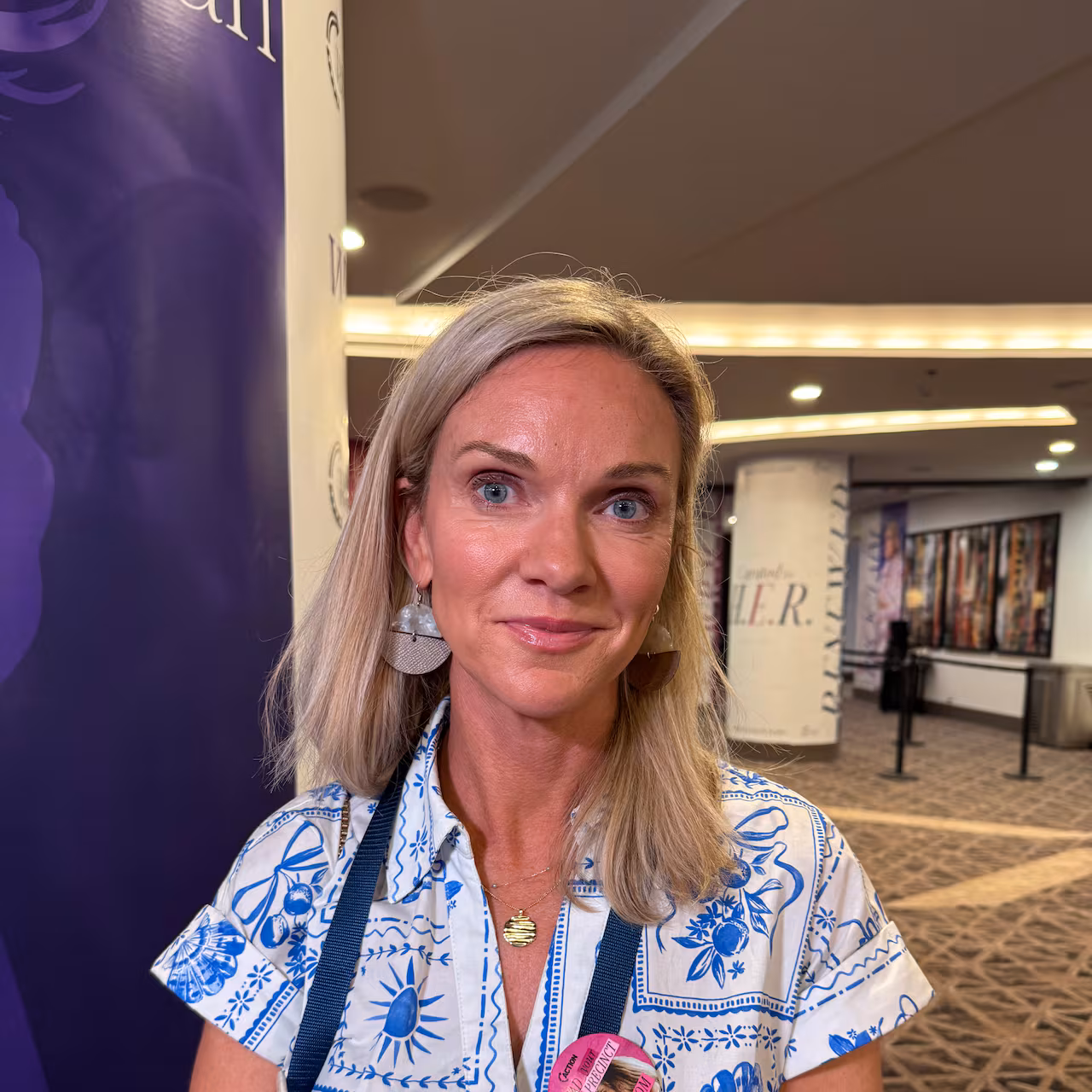 A woman in a white dress with a blue pattern poses for the camera.