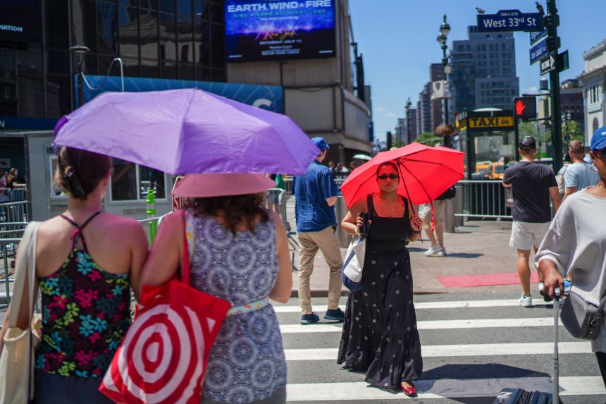Pedestrians using umbrellas to block the sun, cross a street next to Madison Square Garden during extreme heat in New York on Friday, July 3.