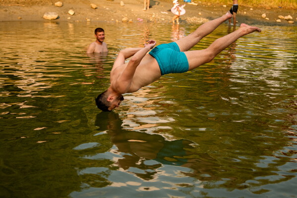A youngster jumps in a river as the National Weather forecaster issued an extreme heat code red warning for most parts of the country, outside 1 Decembrie, Romania, Tuesday, June 30, 2026. (AP Photo/ Andreea Alexandru)