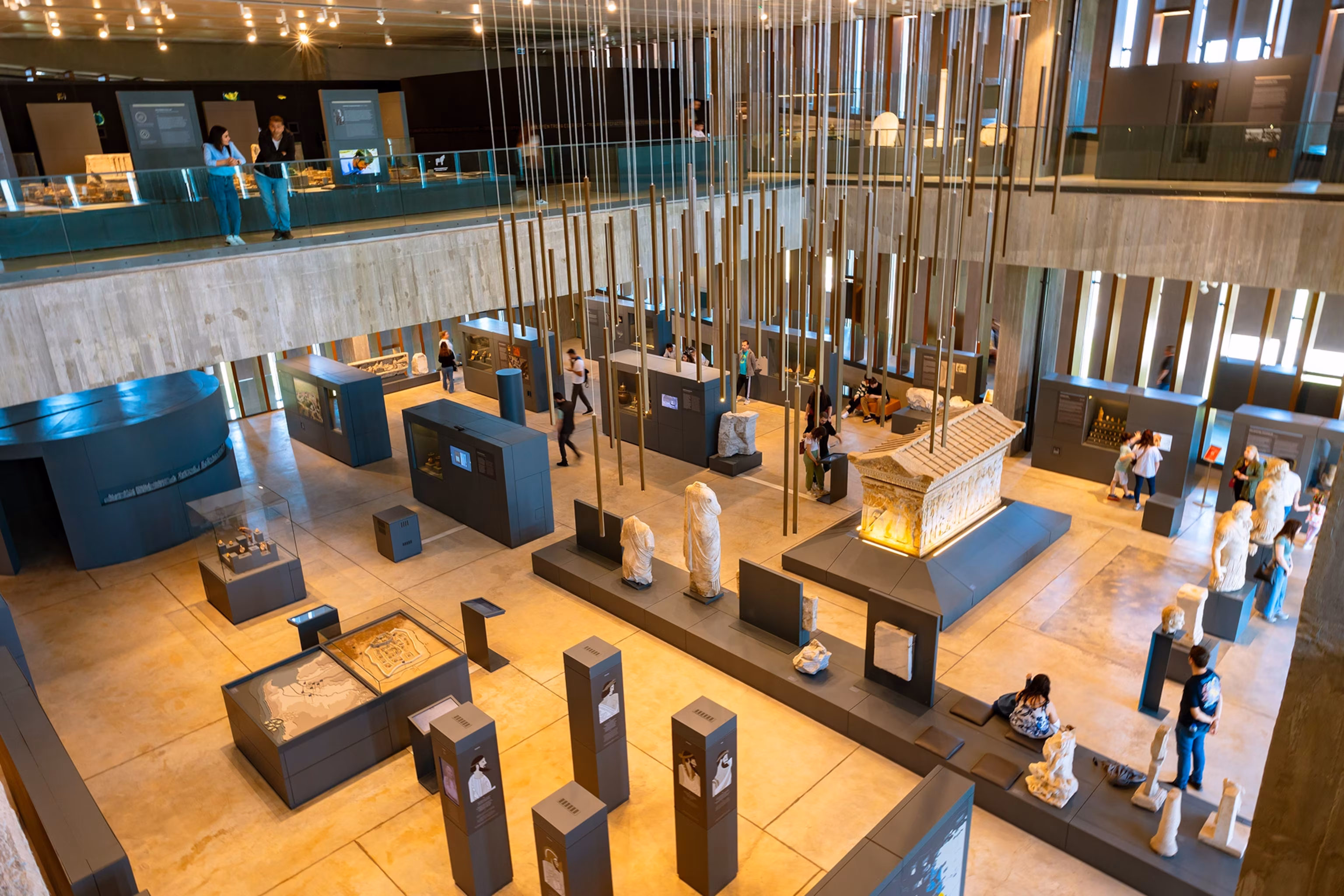 A view from a balcony down into a museum room filled with artifacts and placards and visitors