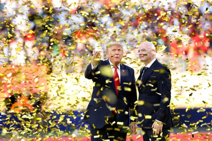 Two people stand amid a shower of gold confetti, dressed in formal suits, at a sports event celebration