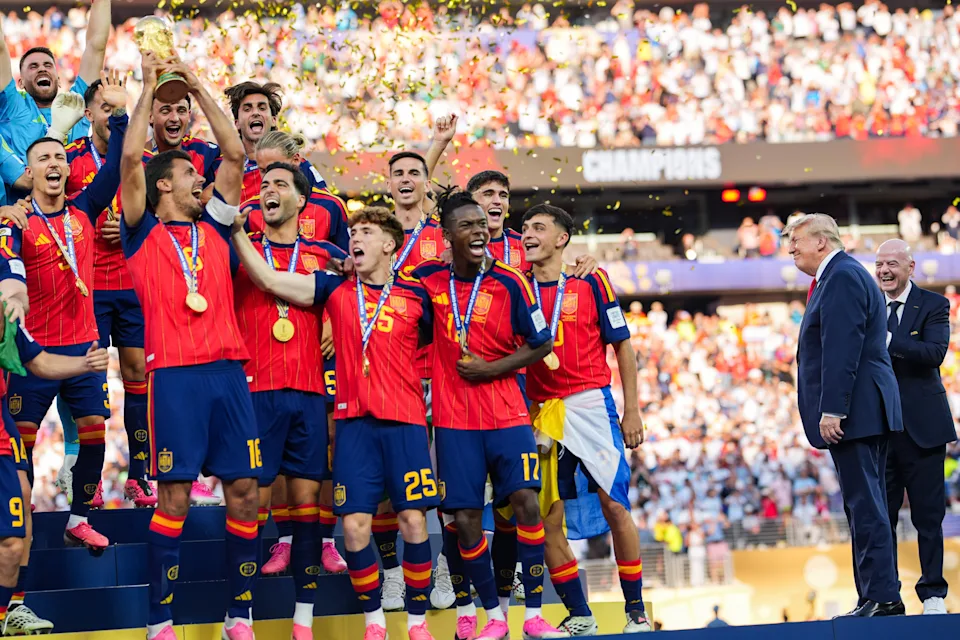 Soccer team celebrates on a podium with medals after a victory; confetti falls and a crowd watches