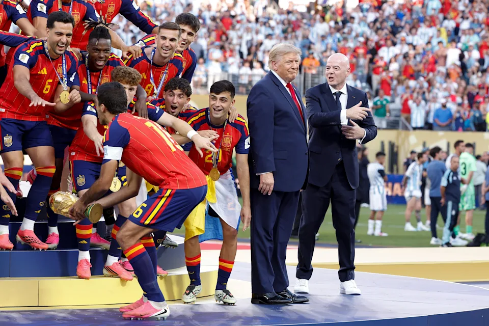 Group of soccer players celebrating on stage with trophies, while two officials in suits stand nearby, during a sports awards ceremony
