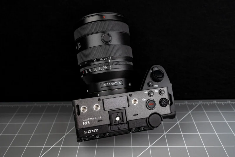 A Sony Cinema Line FX3 camera with a FE 4/20-70 G lens is placed on a gray cutting mat, viewed from above against a black background.