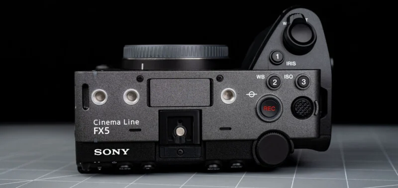 Top view of a Sony Cinema Line FX5 camera body, showing control buttons, dials, REC button, and lens mount, all on a gray grid surface with a black background.