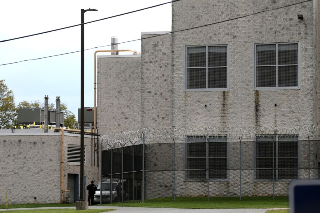 A photo shows a gray brick prison building surrounded by barbed wire fencing.