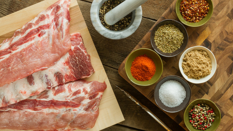 Rack of raw ribs with bowls of various spices in bowls