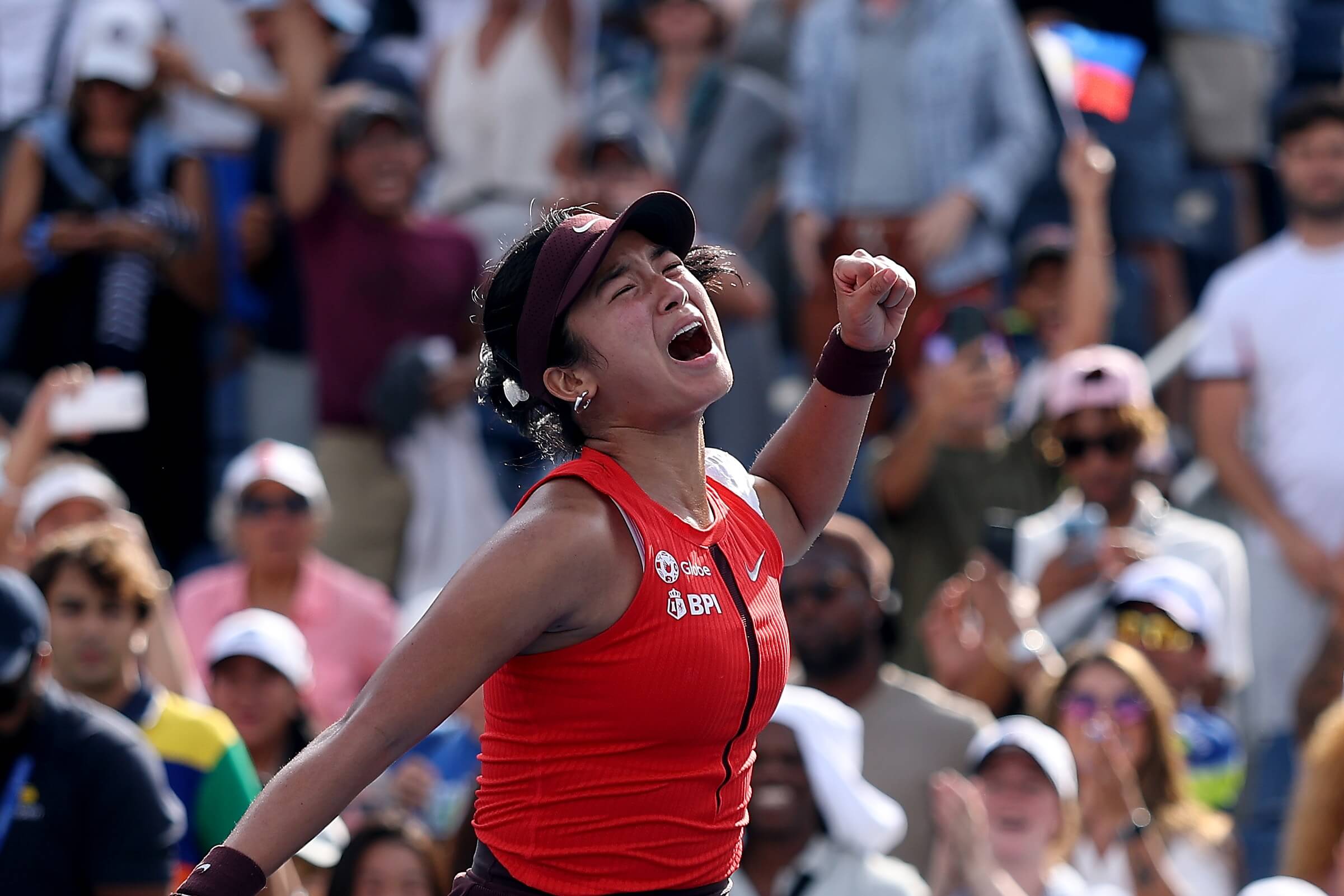 Alex Eala roars in celebration with Filipino flags in a tennis crowd behind her.