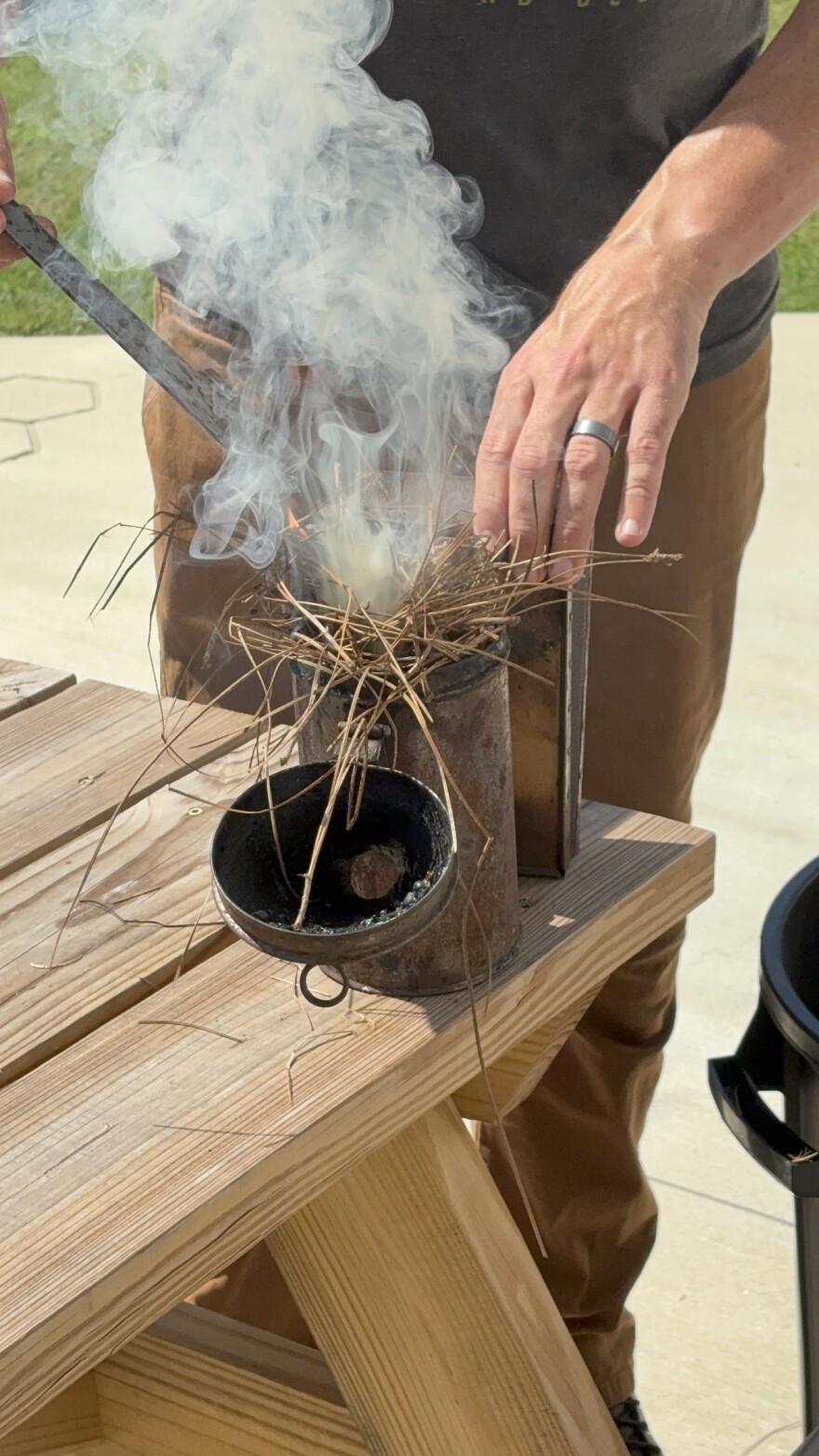 Beekeeper Adam Hickman puts more tinder into a smoker that smoke is already billowing out of.