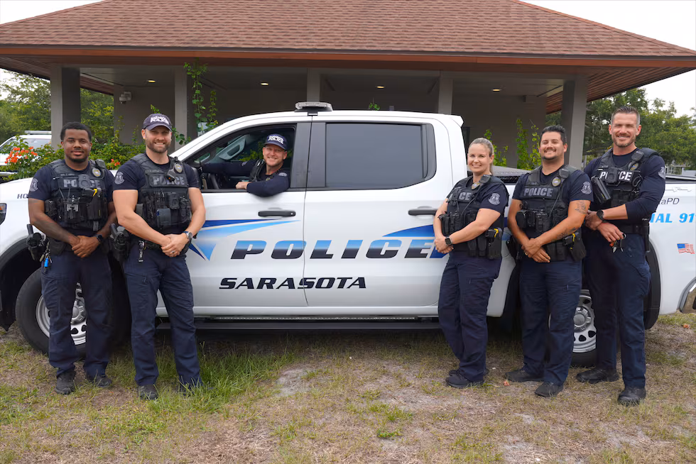 Members of the Sarasota Police Department’s Homeless Outreach Team stand with an SPD vehicle....
