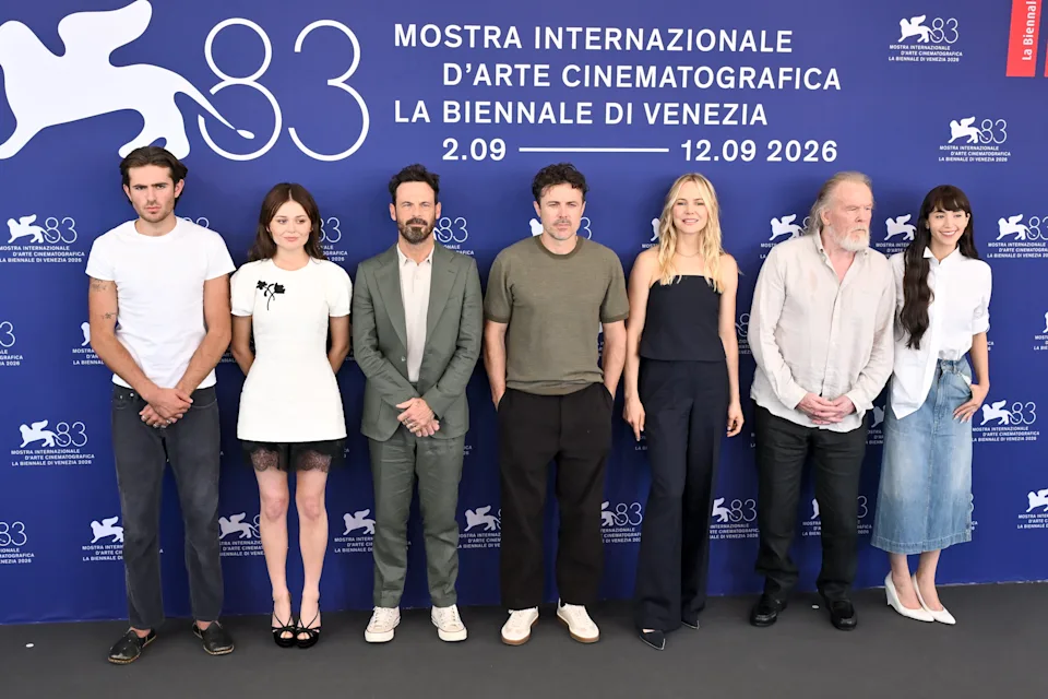 Group of seven people at a film festival, standing in front of a backdrop listing event details. They are in casual to semi-formal attire