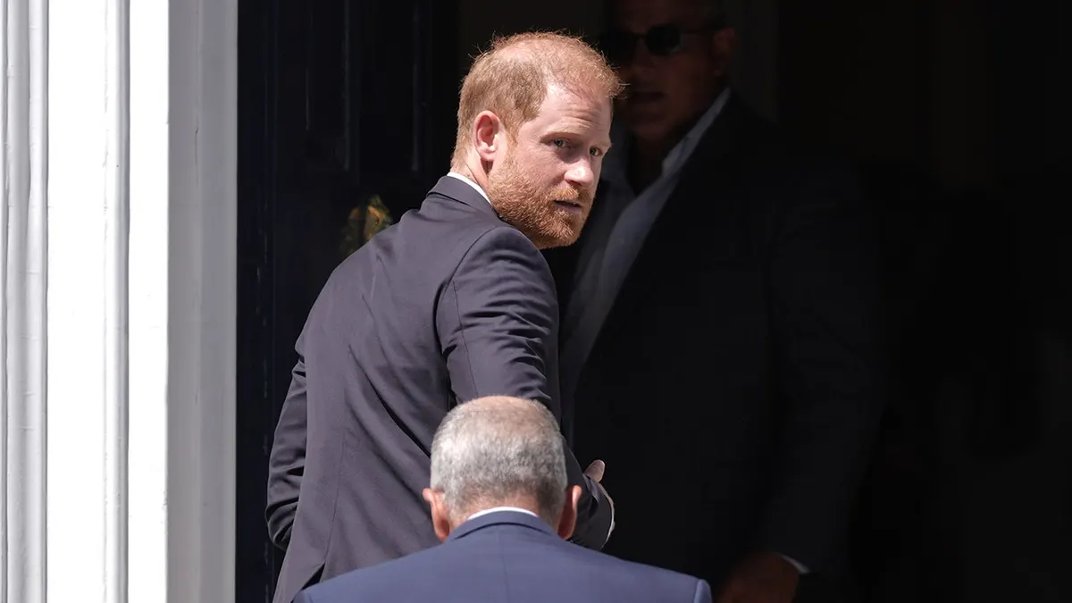 Prince Harry in a dark suit looking from his shoulder as a bodyguard walks in front of him,