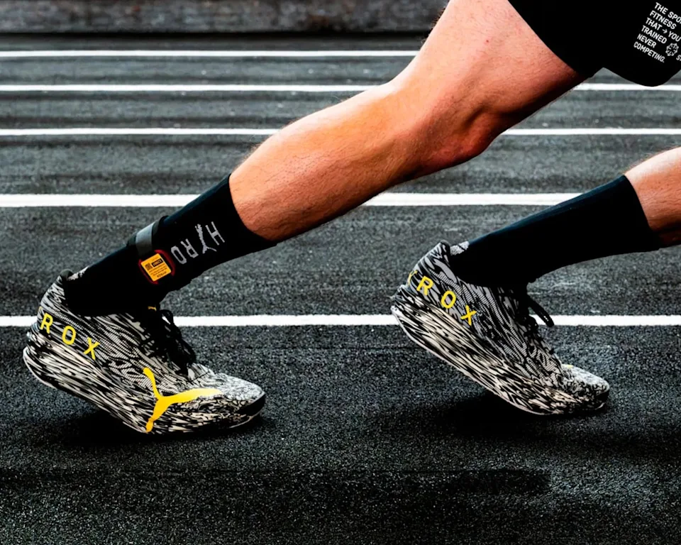 Black running socks and black-and-white patterned sneakers with yellow branding, shown mid-stride on a running track.