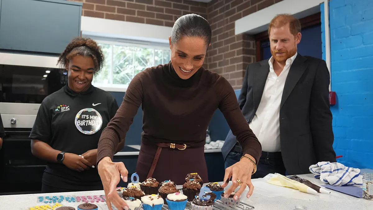 Meghan Markle setting up cupcakes as Prince Harry looks on.