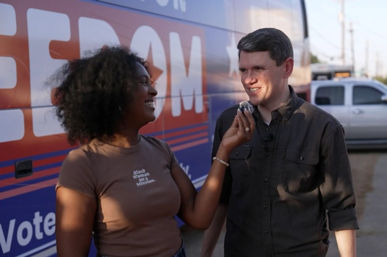 a woman holds a small microphone in front of a man while filming a social video